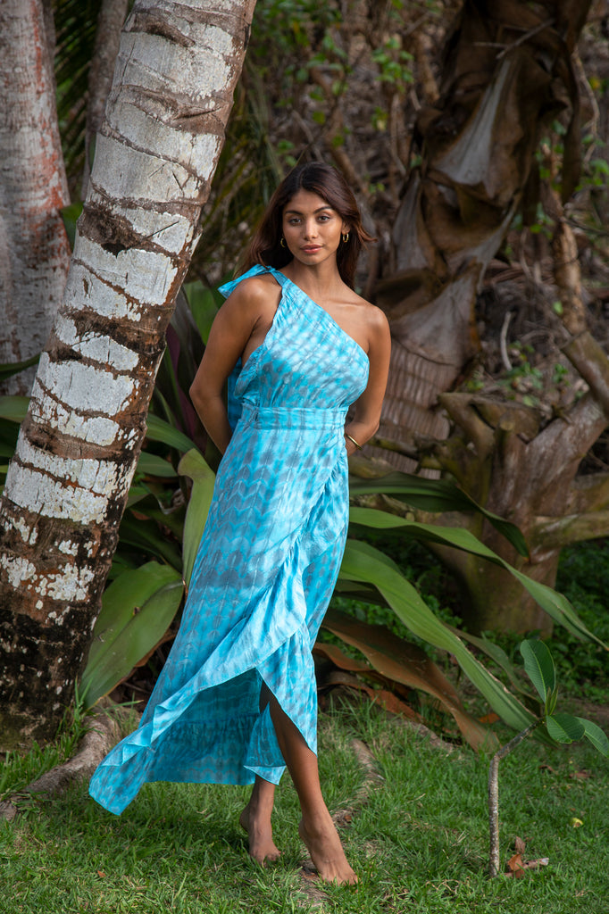 Front of a Woman standing wearing Brianna Convertible Wrap Skirt Dress Looks #4 One shoulder with a belt option in Sophia Loren Turquoise Tie Dye in a garden.