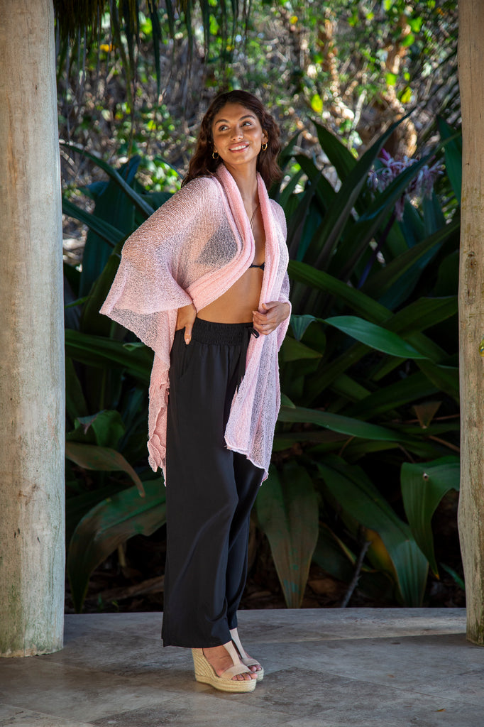 Side of a Woman standing wearing a Summer Knit Long Cardigan Jacket- Kimono Sweater Wrap in Ballerina Pink in front of a forest.