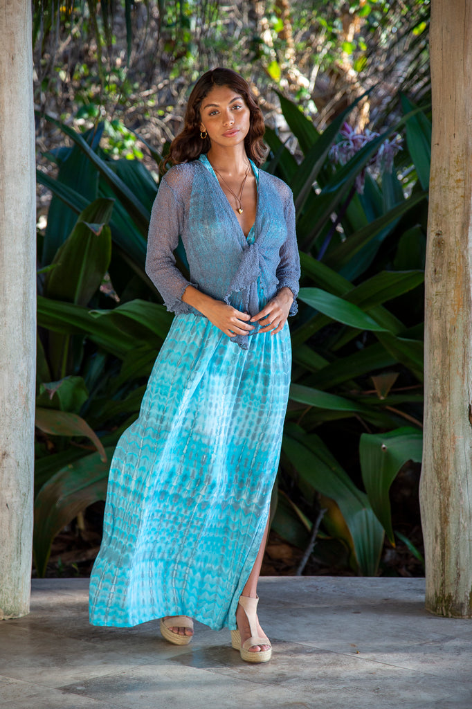 Front of a Woman standing wearing a Summer Knit Cardigan Bolero Shrug Cover in Blue Grey in front of a forest.