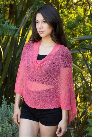 Woman wearing coral pink sheer knit lightweight poncho shawl wrap for resort, wedding, beach, nursing, travel, events, over black outfit and white background