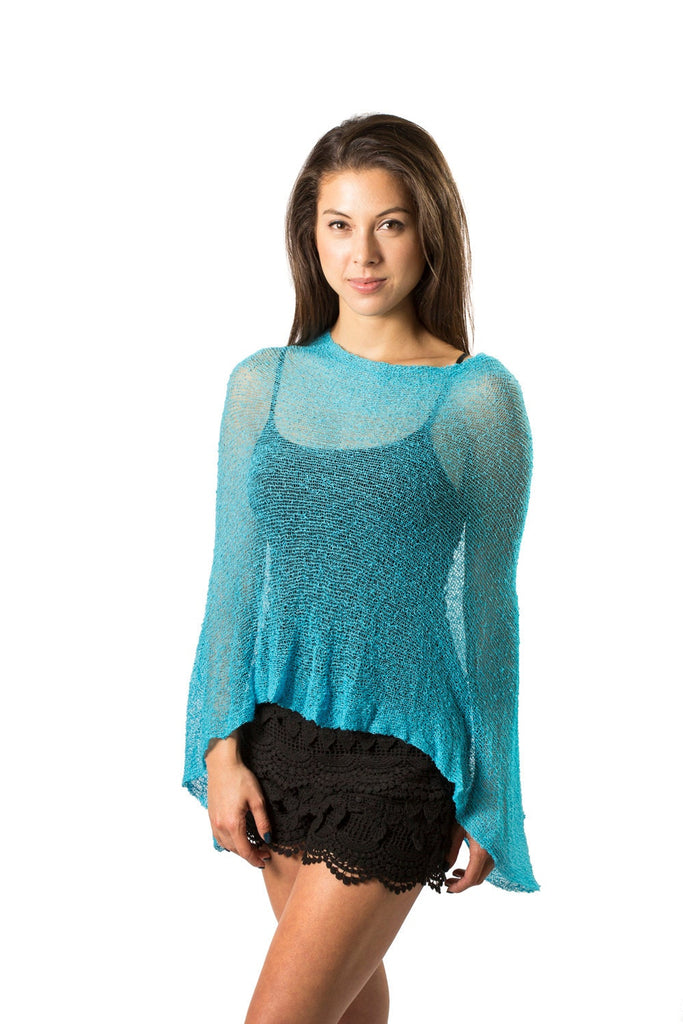 Woman standing upclose wearing Turquoise Blue Knit Poncho Shawl with black shorts against white background